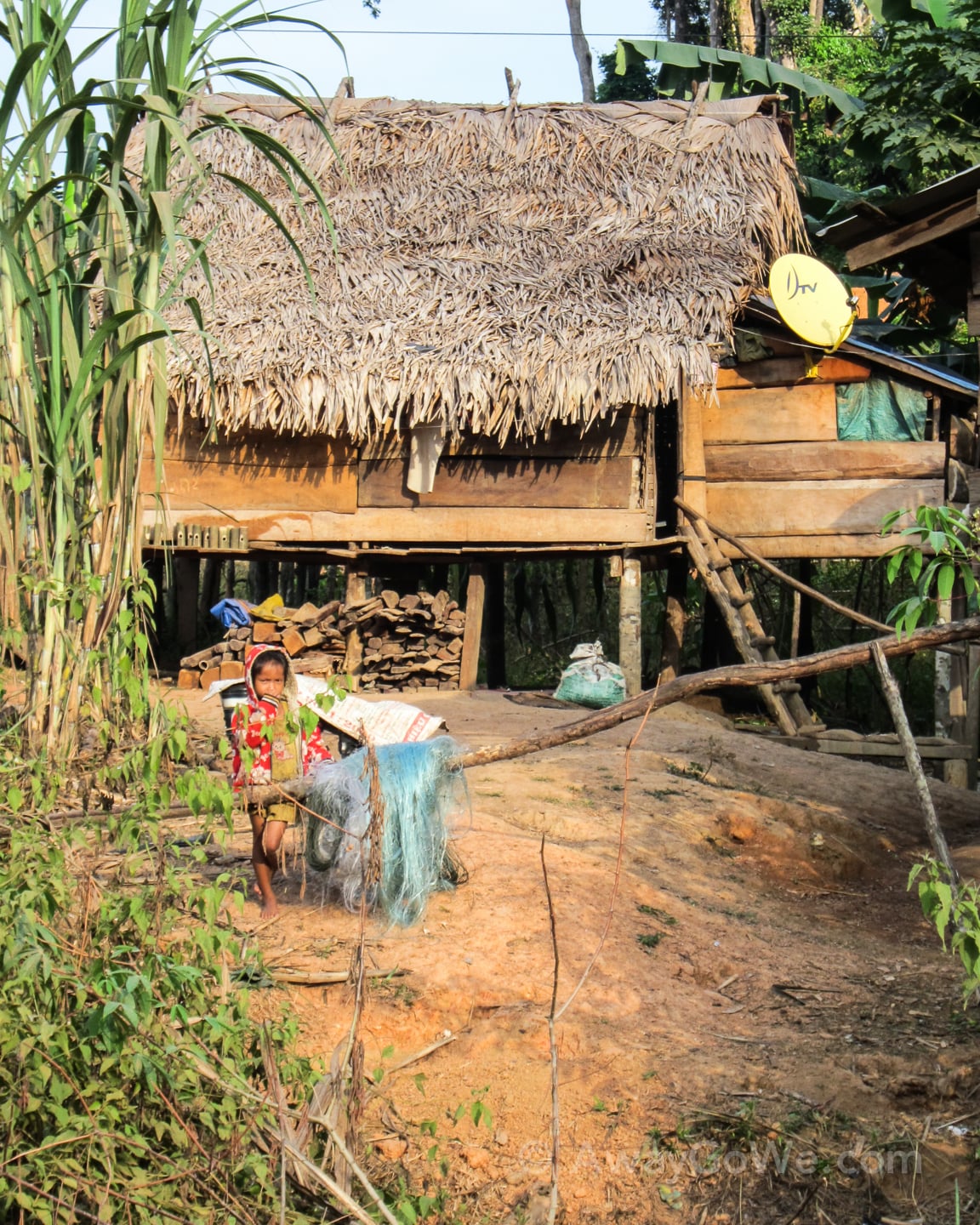 young girl standing in front of traditional wood and thatch house in laos